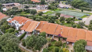 Ett bostadsområde med tak som är täckta av terrakottafärgade tegelpannor, en tennisbana och frodig grönska.