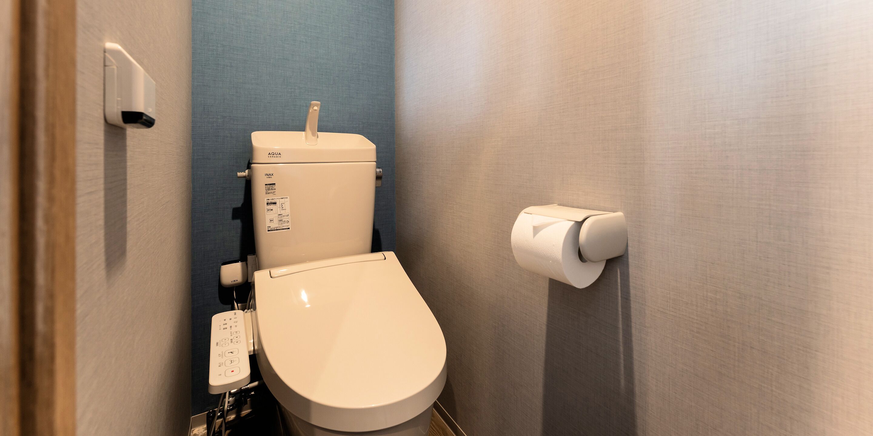 Un inodoro moderno con panel de control, soporte para papel higiénico y botón de descarga en la pared.