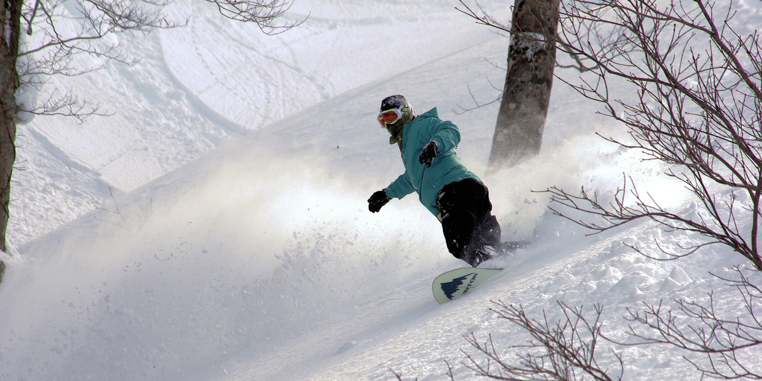 A snowboarder in a teal jacket and black pants on a snowy slope.