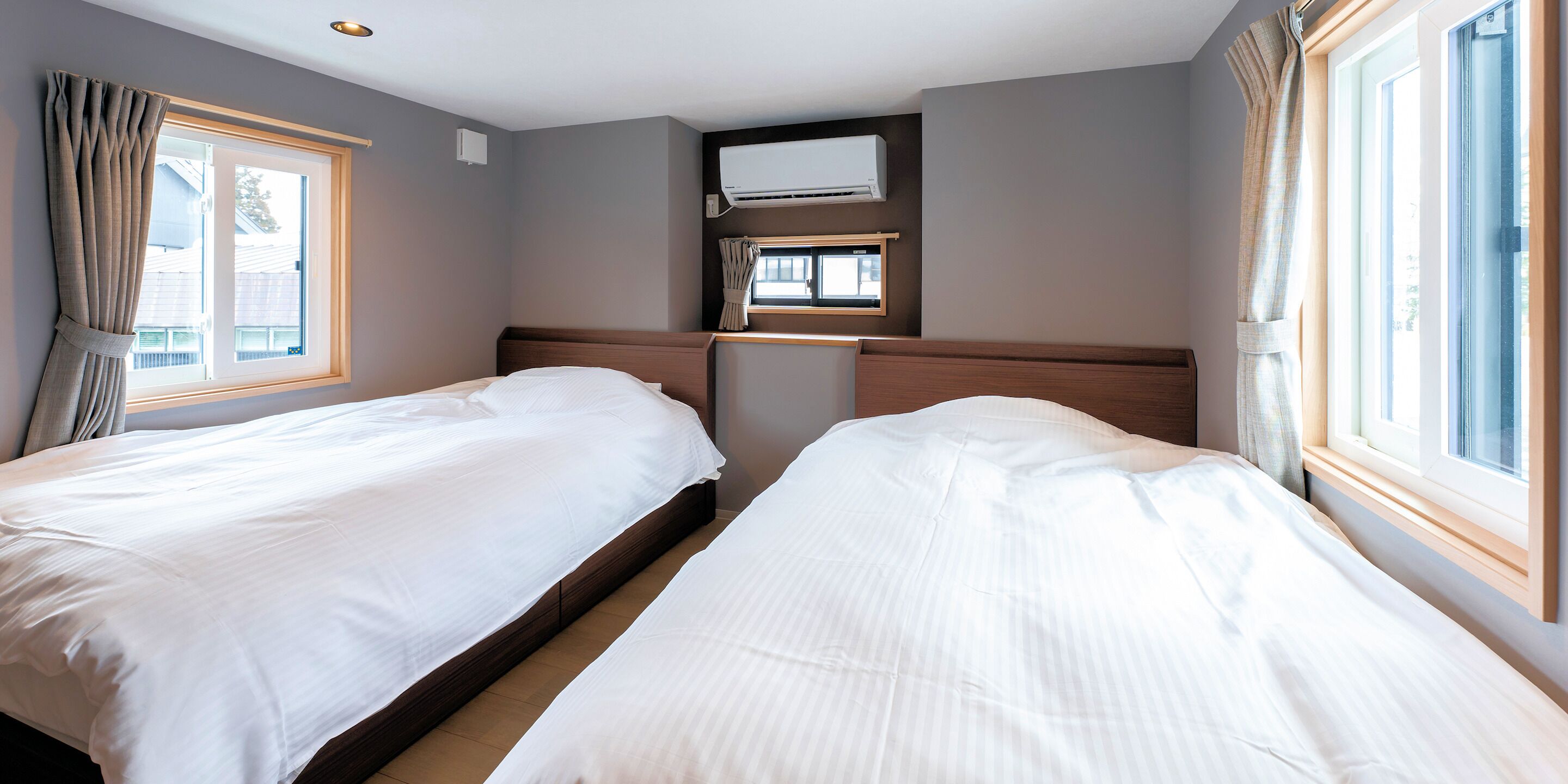 A hotel room with two beds, a window, an air conditioning unit, and a small window above the bed.