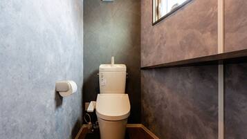 A modern bathroom with a toilet, a hand dryer, and a wall-mounted mirror.