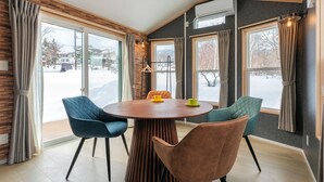A modern dining area with a round wooden table, two blue chairs, and a brown chair. - Myoko Onsen cottage Ajisai  (Myoko)