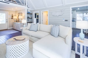 Una sala de estar moderna con un sofá blanco, una mesa de centro de madera y una mesita auxiliar blanca con una lámpara.