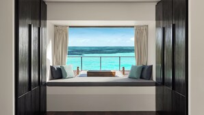 Una habitación con un ventanal grande que da a un mar turquesa, un banco de madera con cojines y paredes de madera oscura.