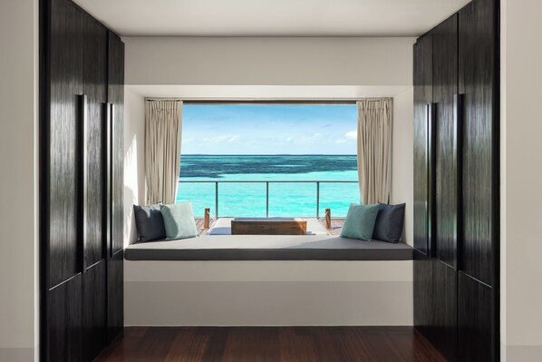 Una habitación con un ventanal grande que da a un mar turquesa, un banco de madera con cojines y paredes de madera oscura.