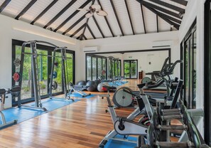 A gym with various exercise equipment, large windows, and a wooden floor.