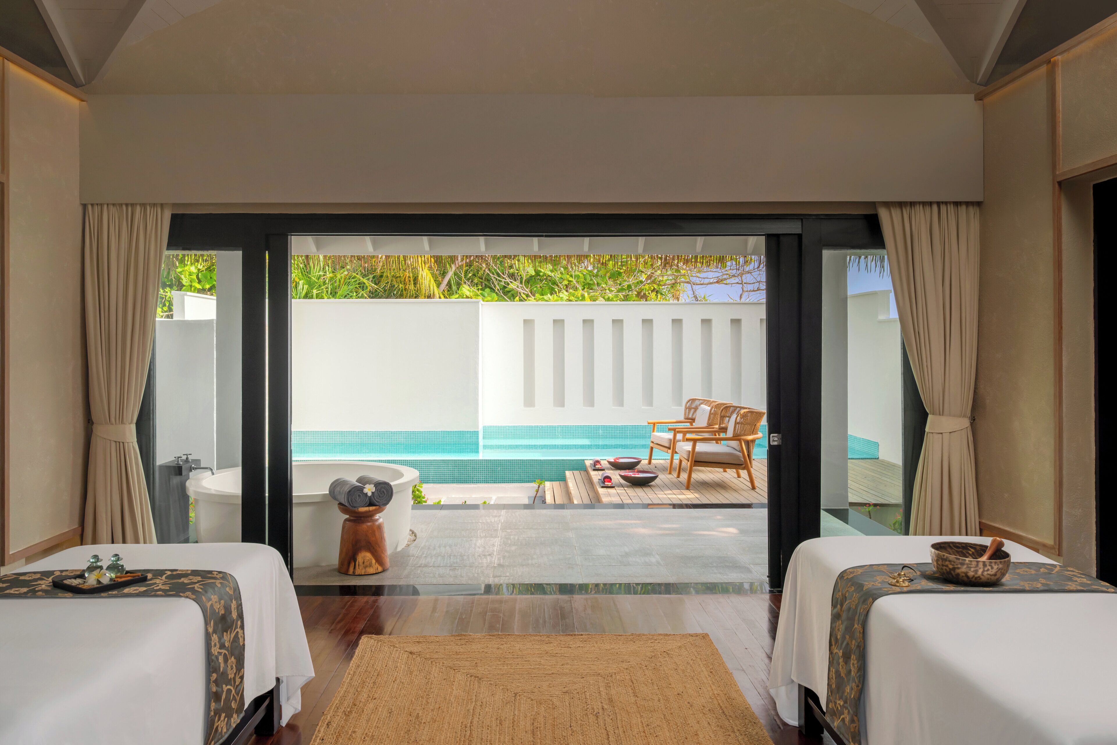 A hotel room with two beds, a view of an outdoor swimming pool, and a wooden deck with chairs.