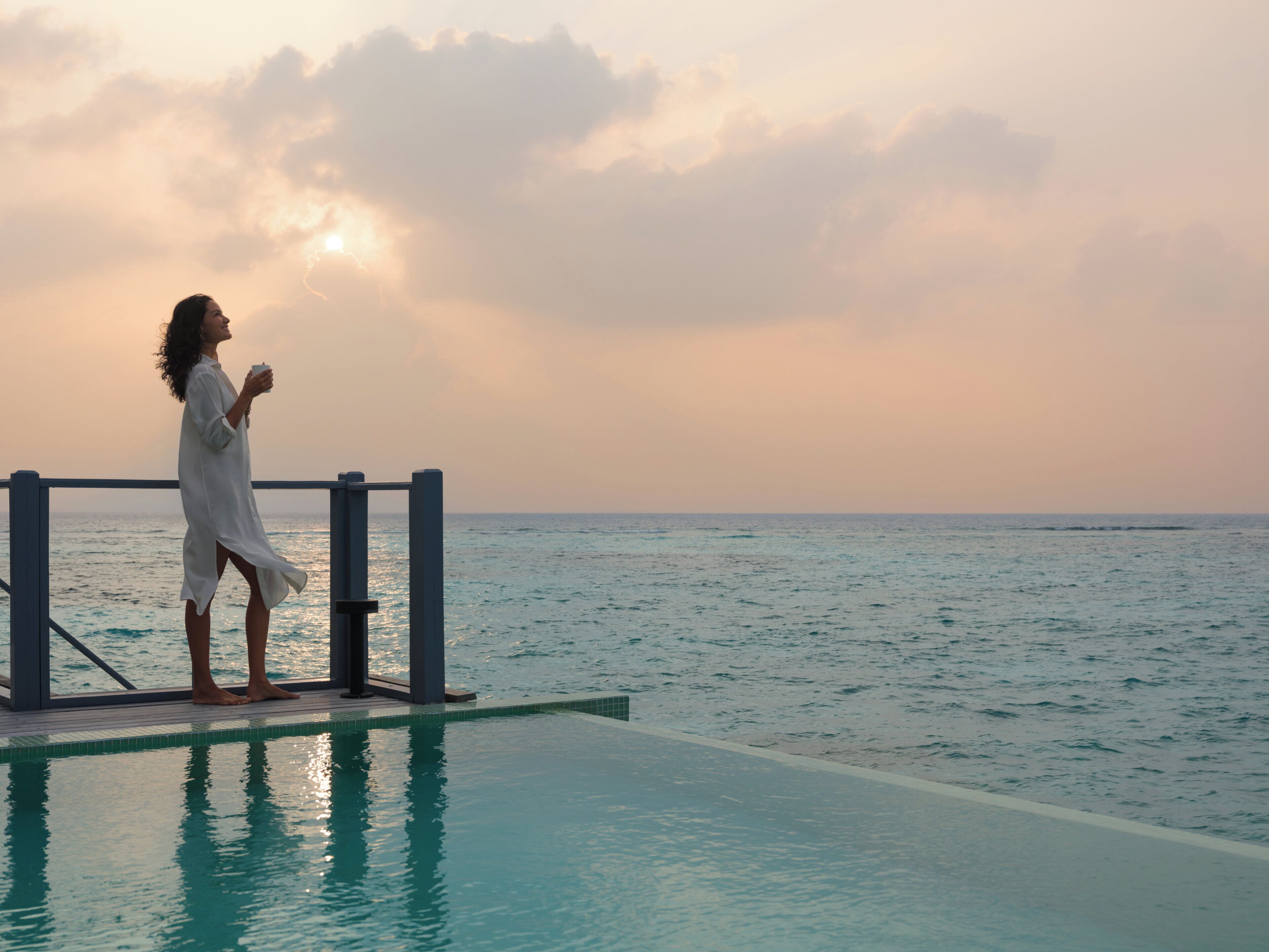 A person standing by a pool with a view of the sea and sky.