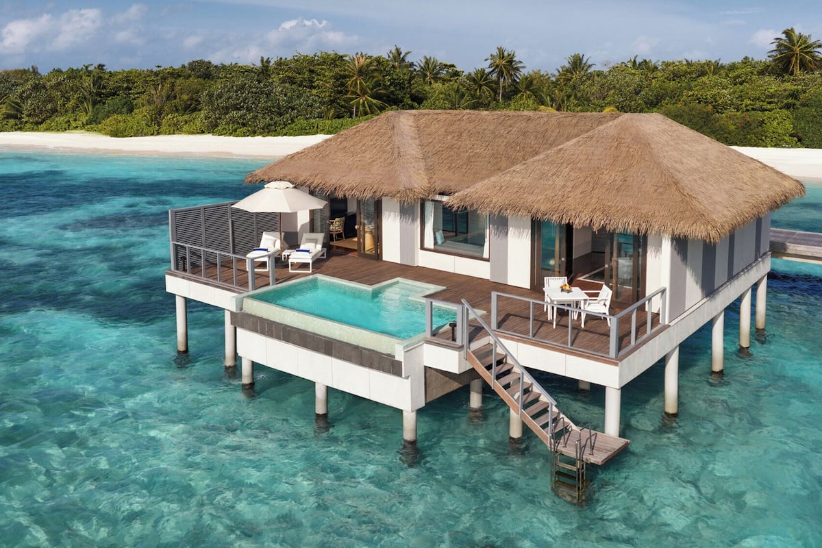 An overwater bungalow with a thatched roof, a pool, and a deck with seating.