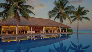 A resort with a pool, palm trees, and a thatched-roof building.