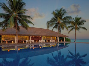 A resort with a pool, palm trees, and a thatched-roof building.