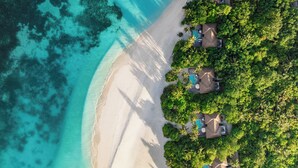 An aerial view of a beach resort with overwater bungalows, clear turquoise waters, and lush greenery.