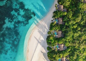 An aerial view of a beach resort with overwater bungalows, clear turquoise waters, and lush greenery.