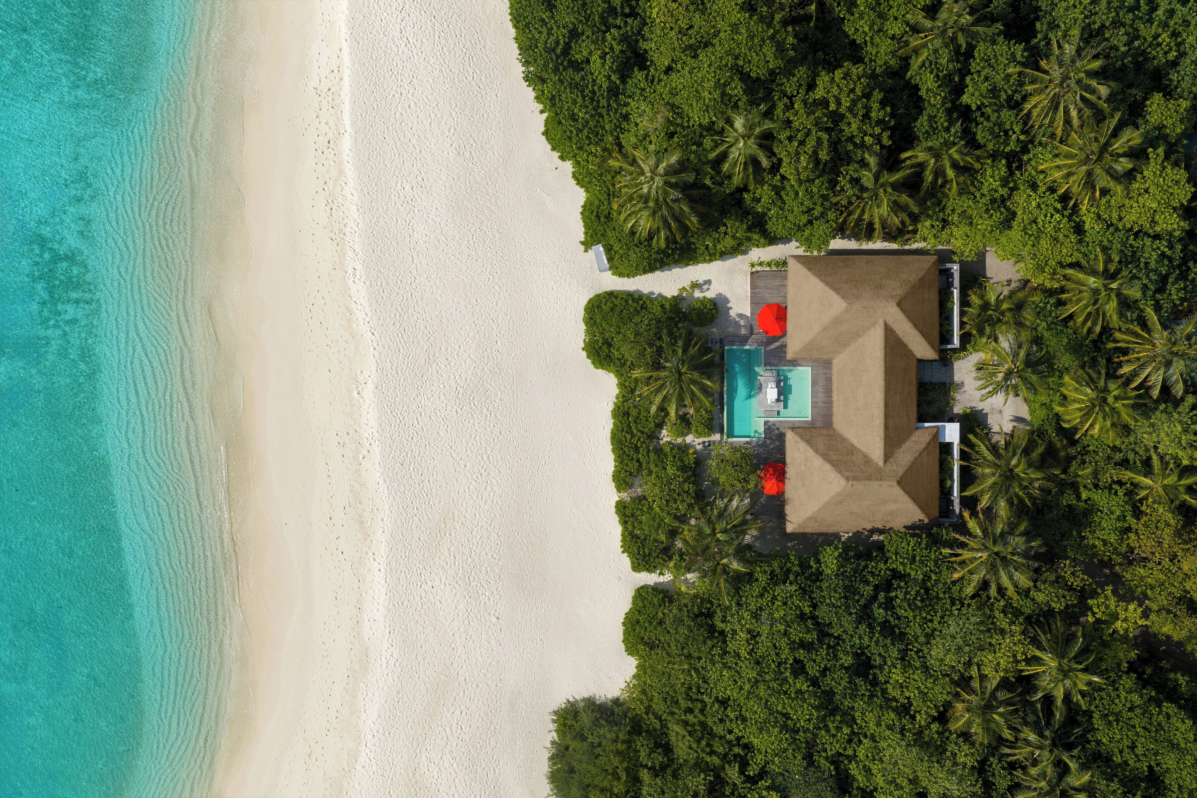 Luchtbeeld van een strandresort met een zwembad, palmbomen en een zandstrand.