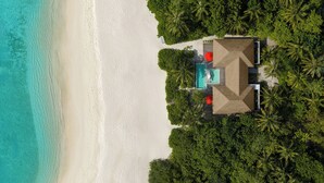 An aerial view of a beachside resort with a swimming pool, palm trees, and a sandy beach.