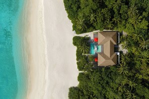 An aerial view of a beachside resort with a swimming pool, palm trees, and a sandy beach.