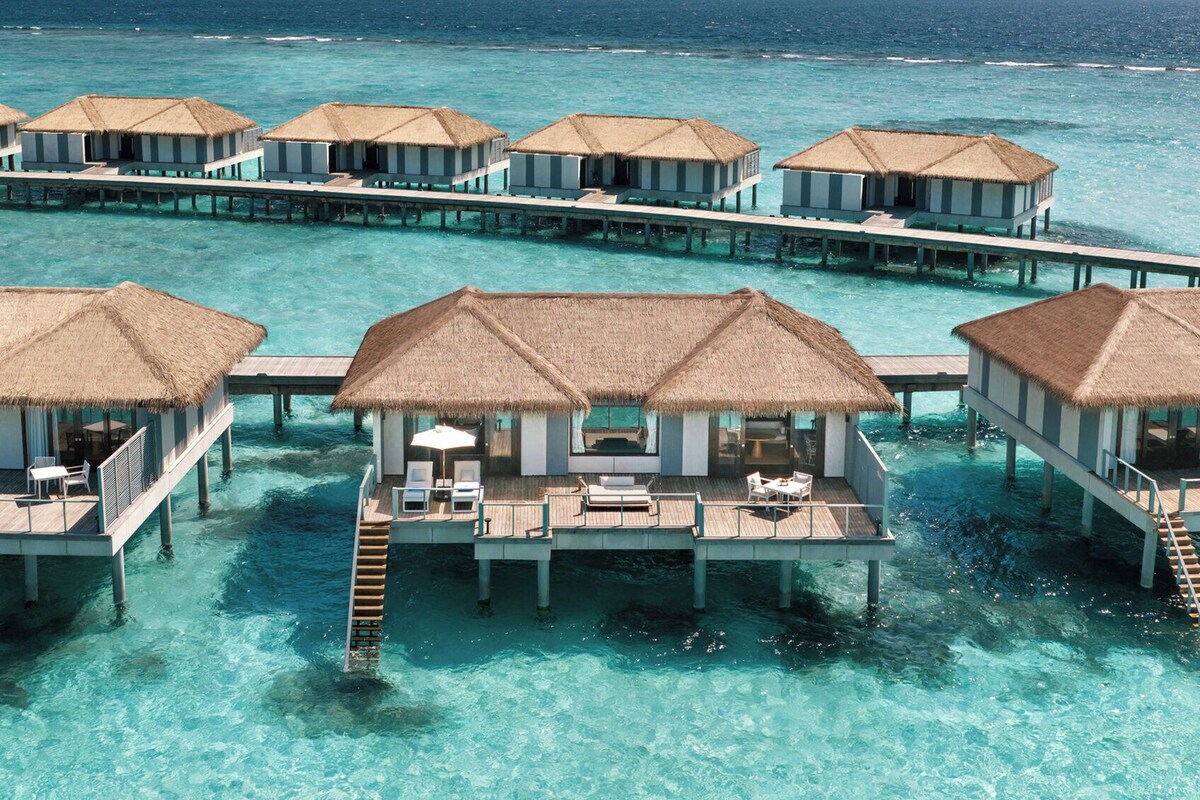 Wasserbungalows mit Strohdächern, Holzstegen und klarem türkisblauem Wasser.