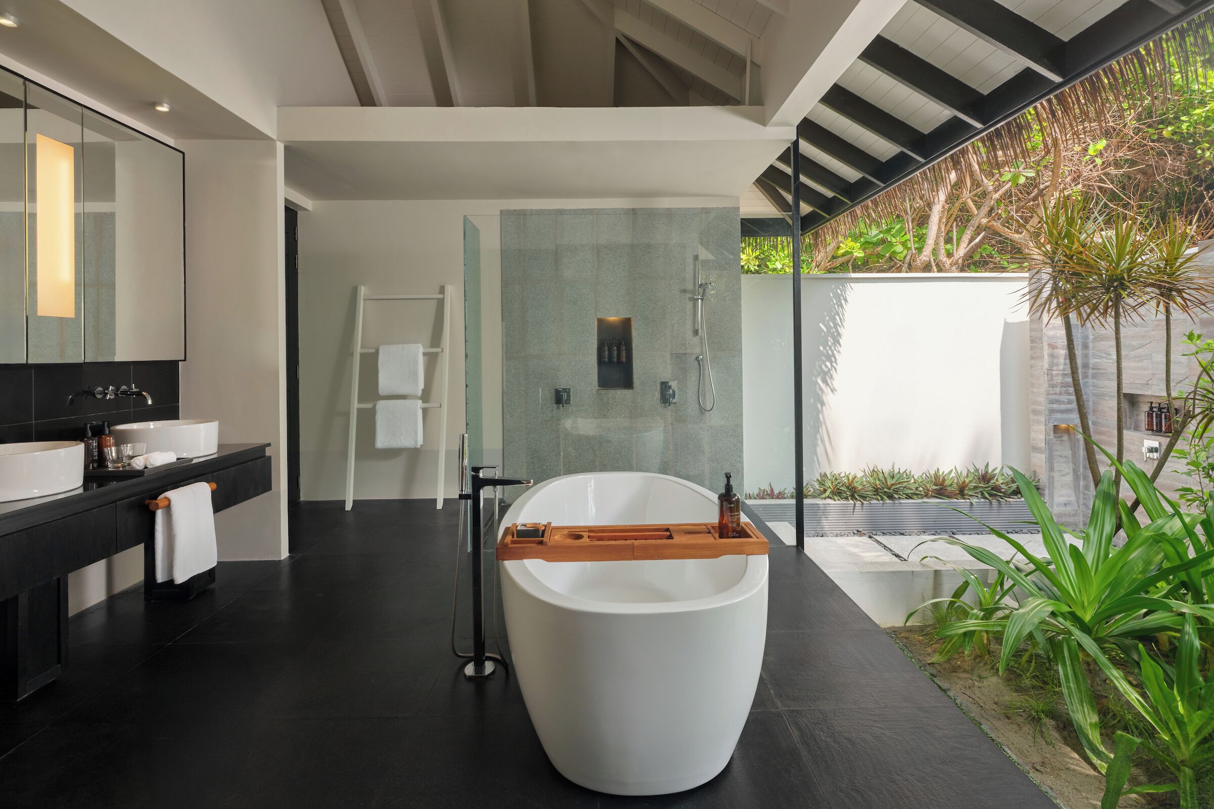 A modern bathroom with a large bathtub, a glass-enclosed shower, and a black countertop with a sink and mirror.