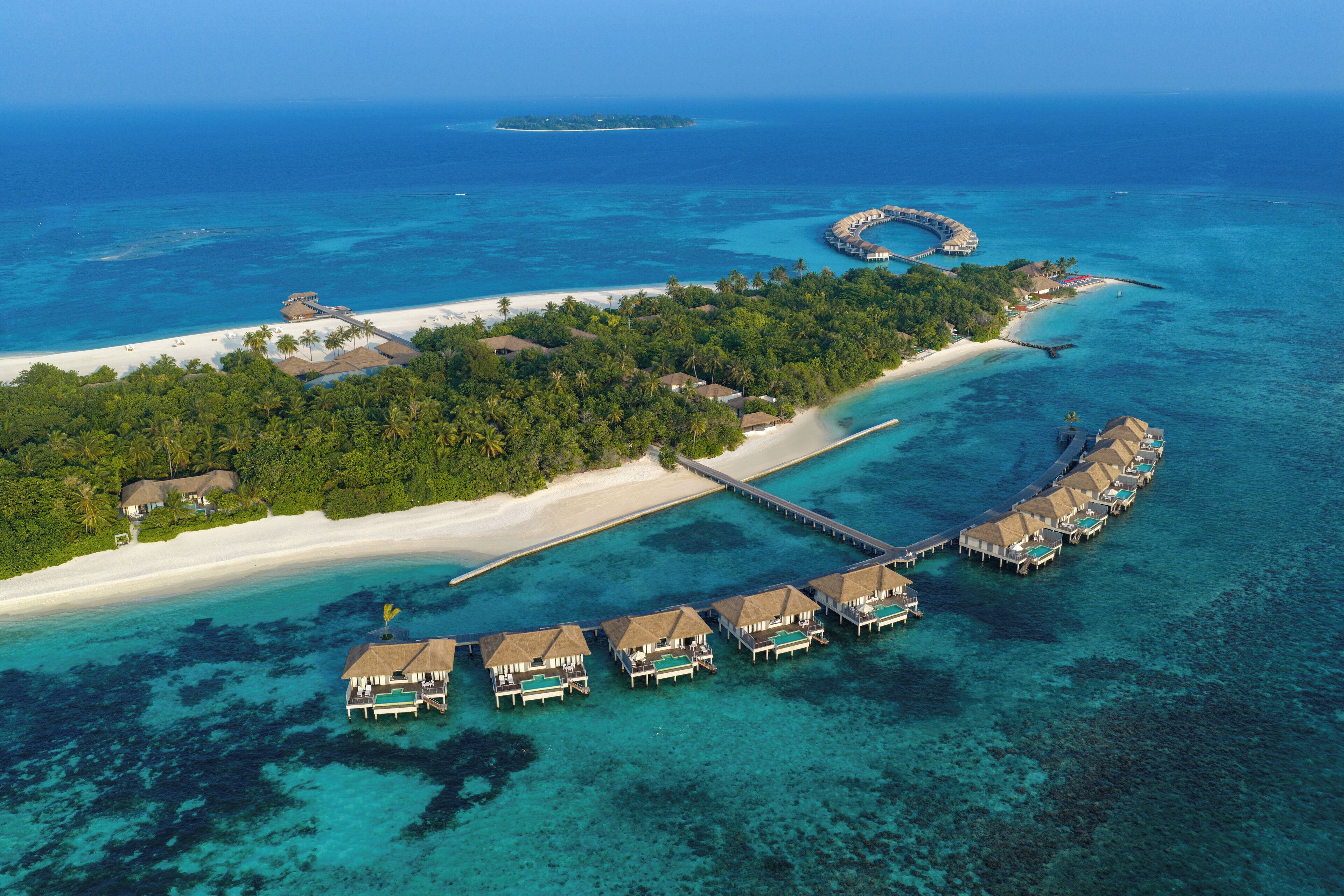 Oversigtsbillede af et resort med overvandingsbungalows, en strand og en mole, der fører til en lille ø.