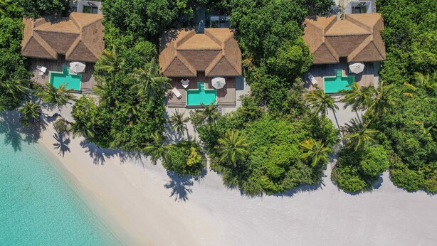 A beachfront property with three thatched-roof villas, each with a private pool, surrounded by lush tropical vegetation.