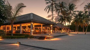 Un resort frente a la playa con estructuras de techo de paja, asientos al aire libre y palmeras.