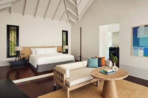 A modern hotel room with a large bed, a sofa, a round wooden table, and a mirror.