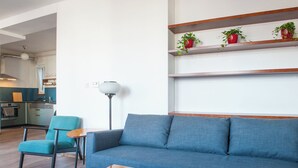 A modern living room with a blue sofa, a wooden coffee table, and a teal armchair. There are red potted plants on a wooden shelf above the sofa. - Spacious 2-bedroom 2 story loft near Opera/Andrassy with AC, WiFi (Budapest)