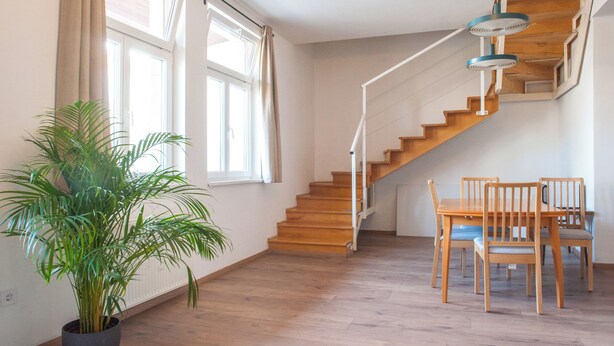 A staircase with wooden steps and a white railing, leading to a landing with a dining table and chairs. - Spacious 2-bedroom 2 story loft near Opera/Andrassy with AC, WiFi (Budapest)