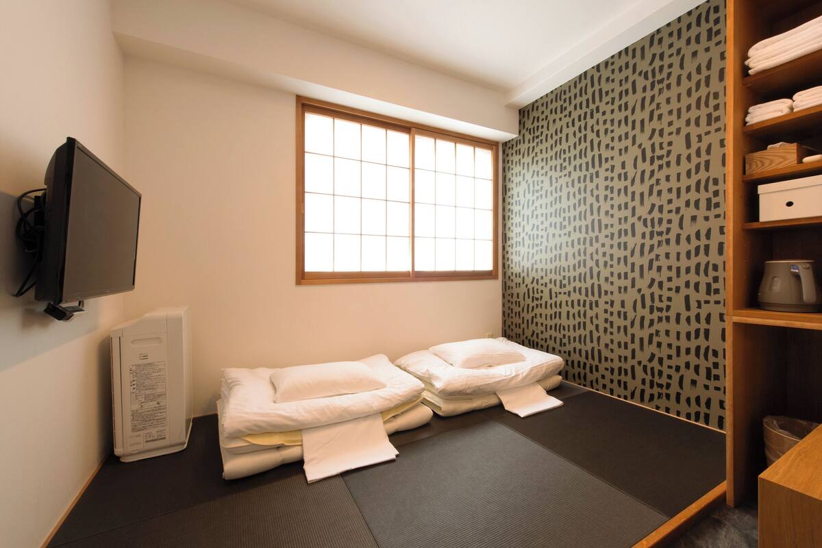 Ein kleines Zimmer mit zwei Betten, einem Fernseher, einer Heizung und einem Fenster.