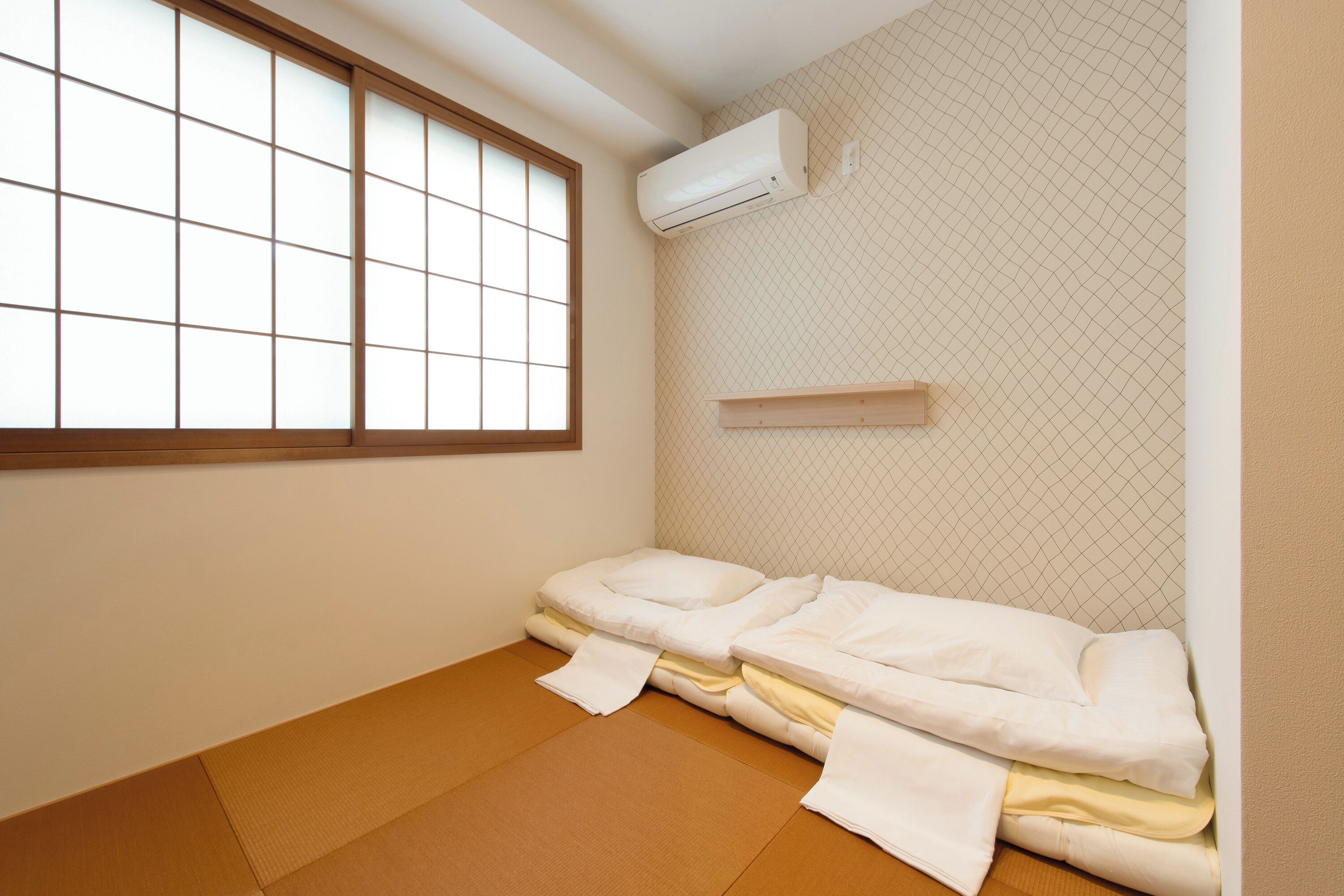 A room with tatami flooring, a futon bed, a window with a grid pattern, and a wall-mounted air conditioner.
