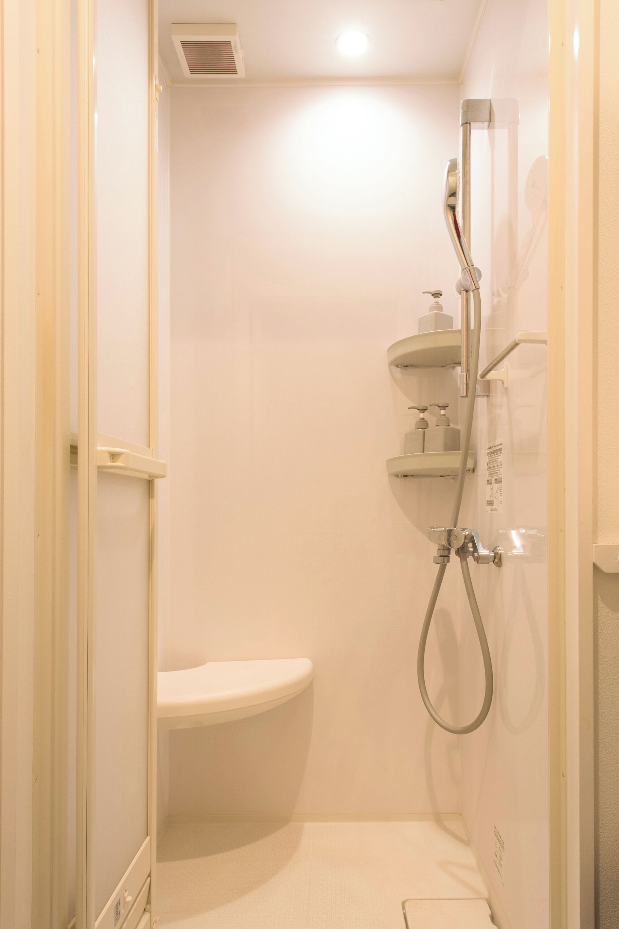 A small, enclosed shower area with a toilet, a handheld showerhead, and a wall-mounted faucet.