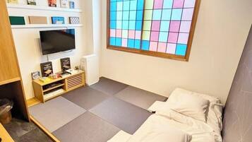 A compact room with a bed, a television, a small desk, and a window with a colorful view.