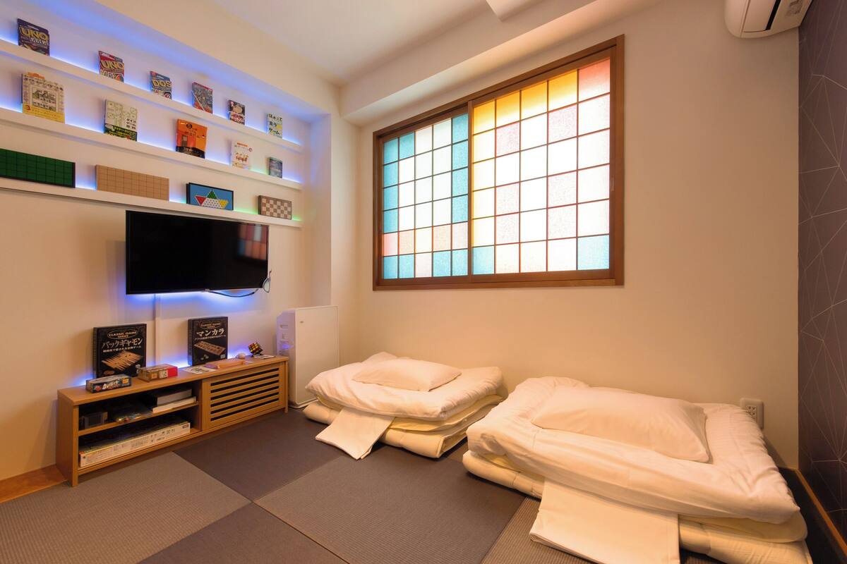 Ein Zimmer mit Fernseher, Regalen mit Büchern und Spielen, zwei Betten und einem Fenster mit Blick.