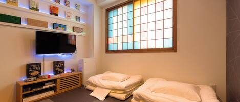 Habitación con televisión, estanterías con libros y juegos, dos camas y ventana con vistas.