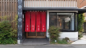 A building with a wooden fence, red curtains, and a small garden area. - Fushiginayado (Kyoto)