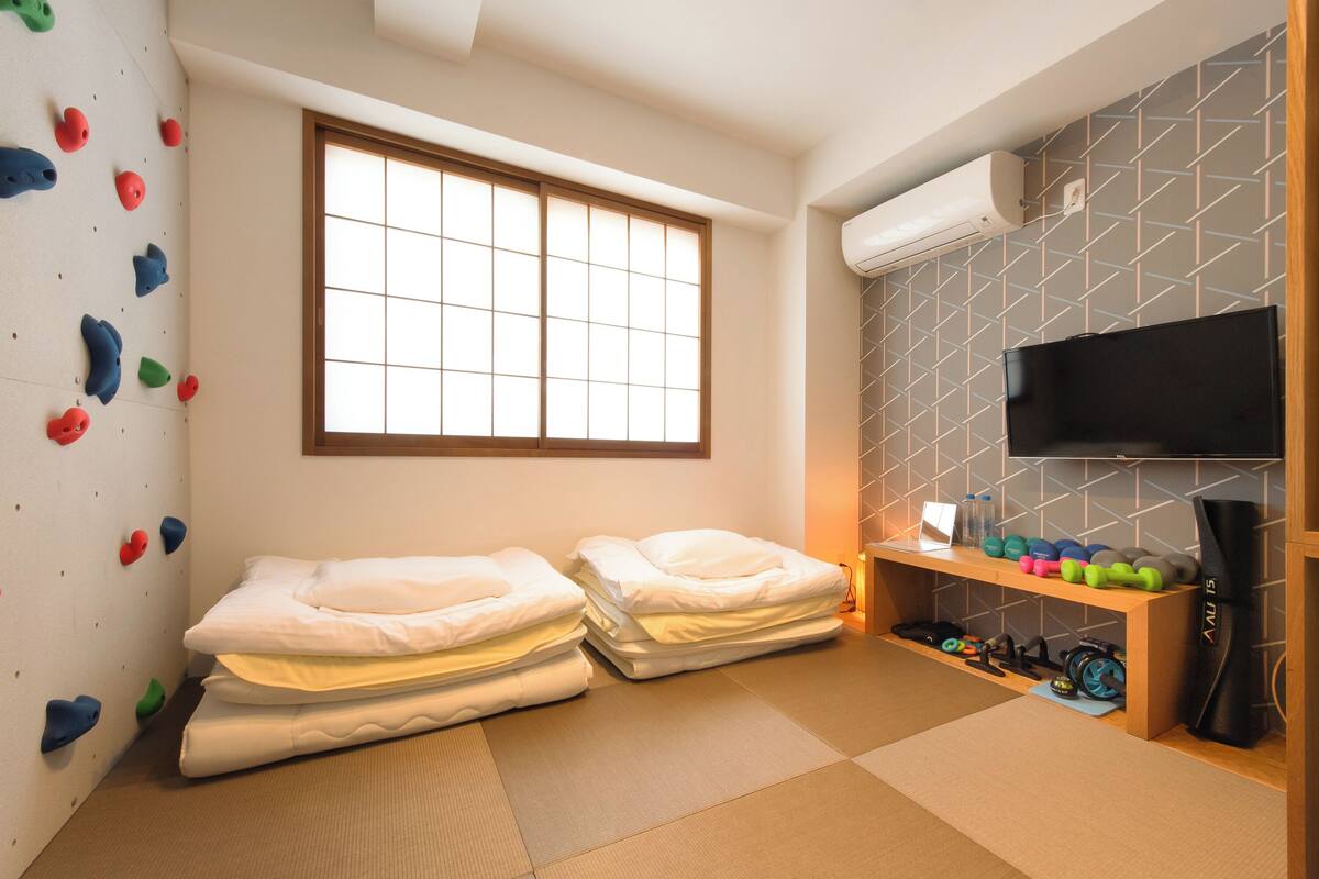 Ein Zimmer mit zwei Betten, einer Kletterwand, einem Fernseher und einem Regal mit Trainingsgeräten.
