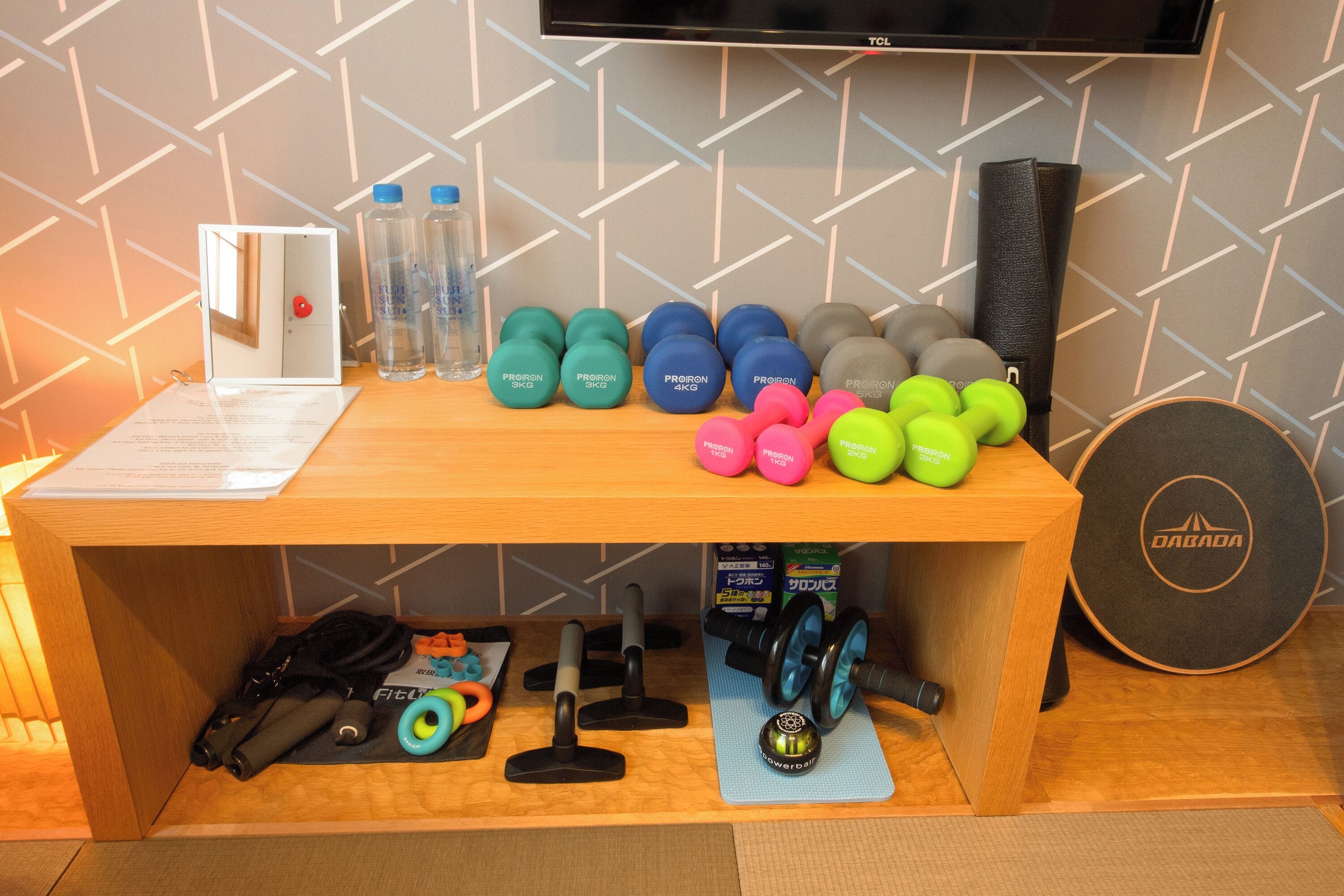 Ein Holztisch mit Trainingsgeräten, darunter Kurzhanteln, ein Spiegel und eine Matte.