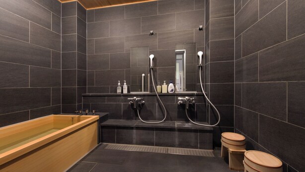A modern bathroom with a wooden bathtub, a shower with a handheld showerhead, and two wooden stools. - Fushiginayado (Kyoto)
