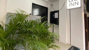 Un espace d’accueil avec une enseigne « GO INN », des plantes en pot, une porte noire et un sol carrelé.