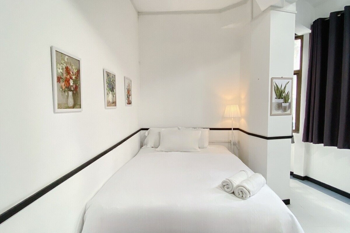 Ein Hotelzimmer mit einem großen Bett, weißen Wänden und schwarzem Rahmen. An der Wand hängen drei gerahmte Bilder und auf dem Nachttisch steht eine Lampe.