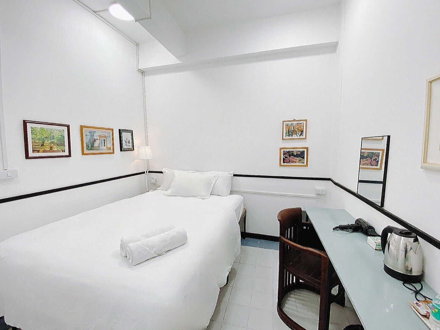A hotel room with a bed, a desk, and a chair. There are framed pictures on the wall.