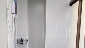 Une petite salle de bain compacte, équipée d’une douche, de toilettes et d’une serviette posée sur le sol.