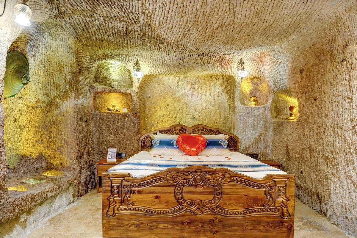 Ein Schlafzimmer mit einem hölzernen Bett, einem herzförmigen Kissen und Steinwänden.