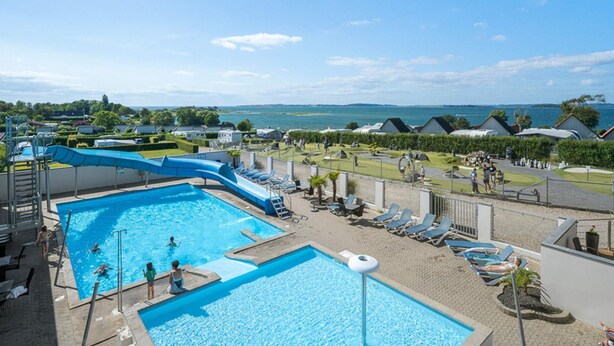 A pool area with two swimming pools, lounge chairs, and a view of the sea. - 6 Person Holiday Park Home in Faaborg (Faaborg)