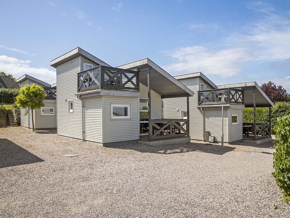 A row of modern, single-story cabins with large windows and balconies, set on a gravel ground with a clear sky.