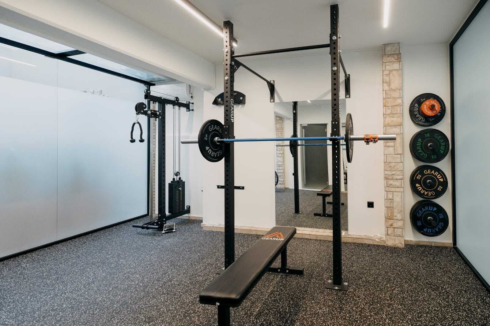 Une salle de sport équipée d’un support à squats, d’un banc et de poids.