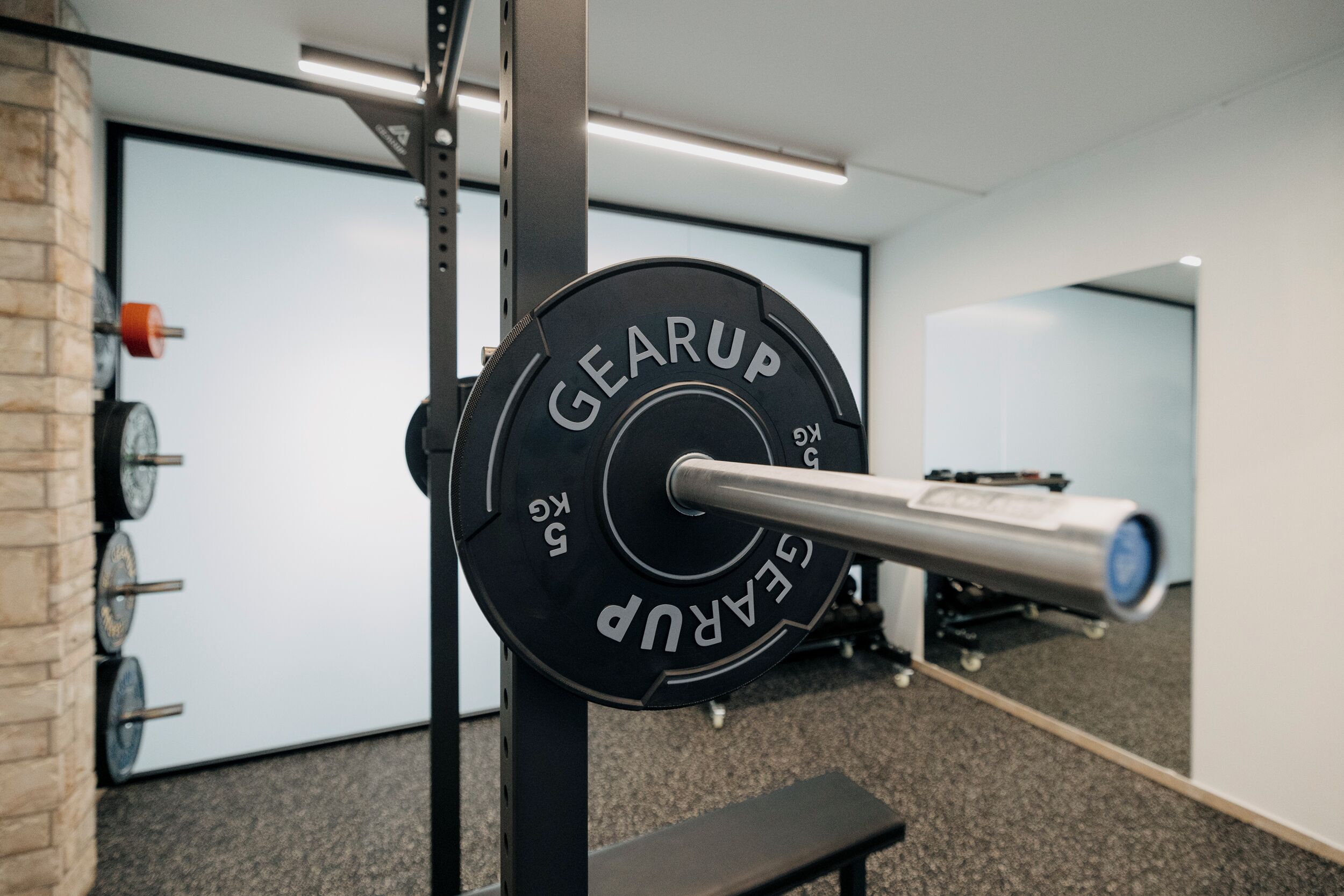 En ställning för tyngdlyftning med en skivstång märkt med texten ”GEARUP” i ett gym.