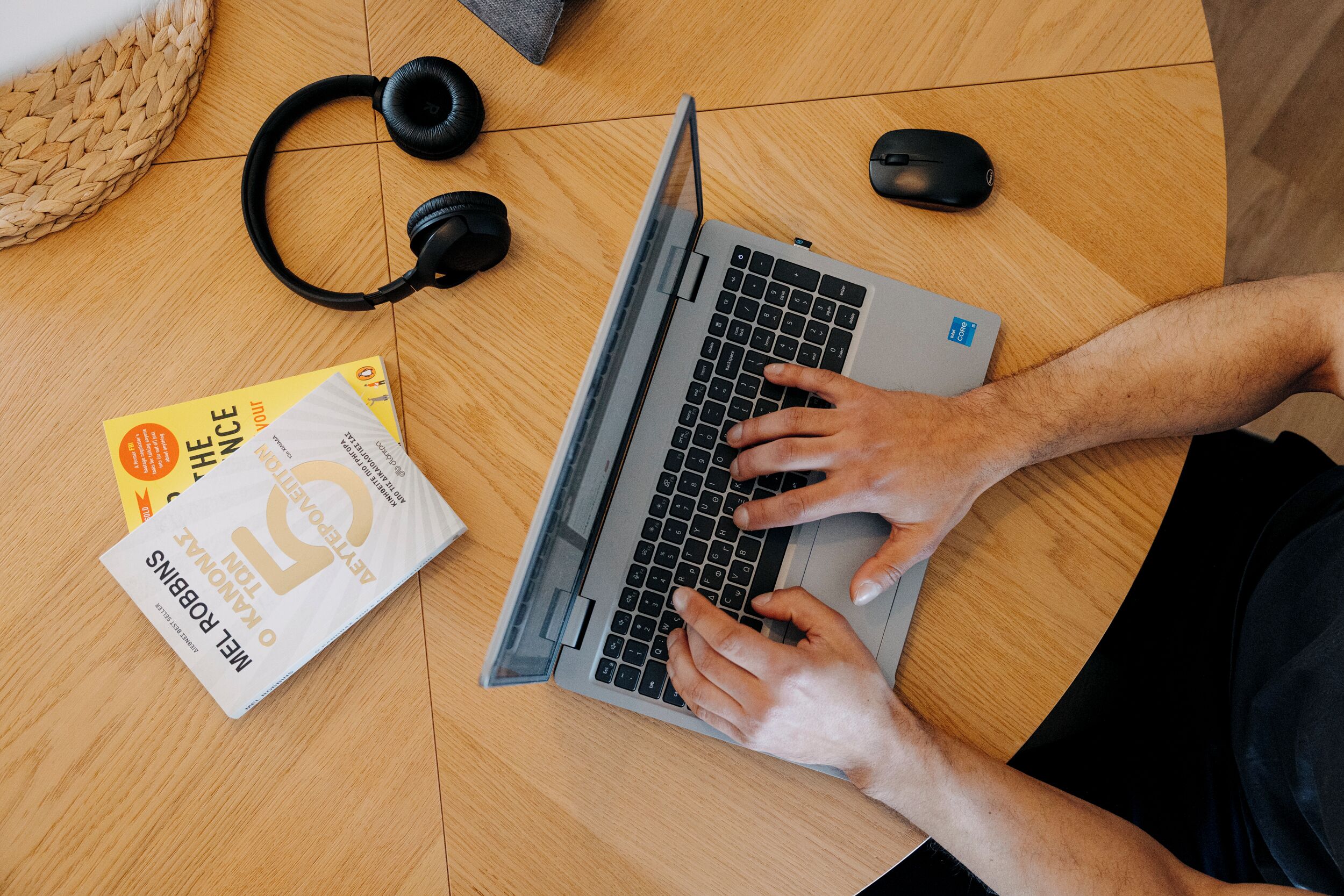 A laptop on a wooden table with a pair of headphones, a mouse, and a book.