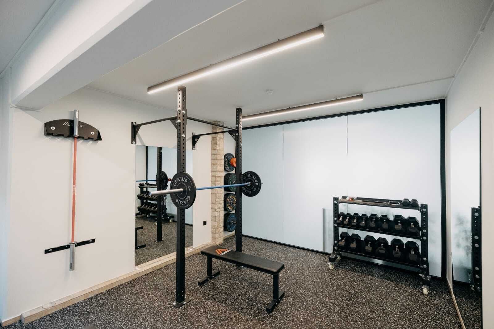 A gym with a squat rack, bench, and dumbbells.