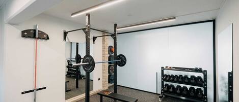 A gym with a squat rack, bench, and dumbbells.